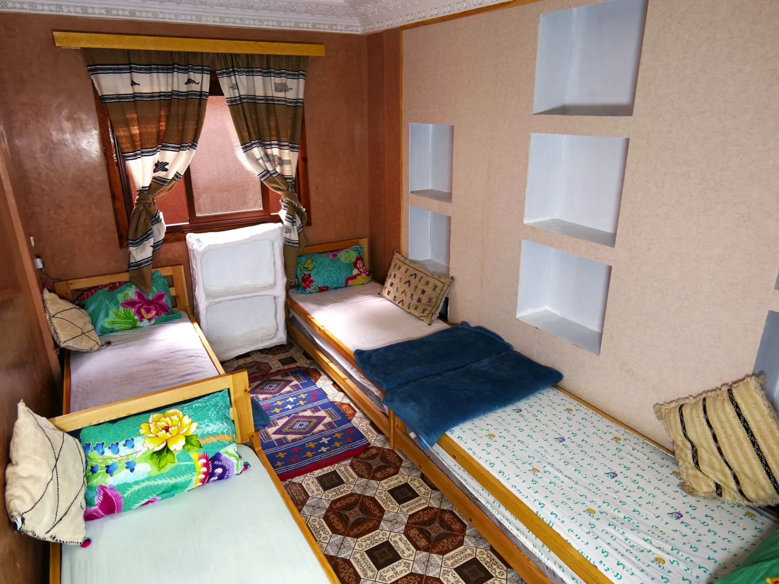 Female dorm with single beds, bright bedspreads and a patterned rug