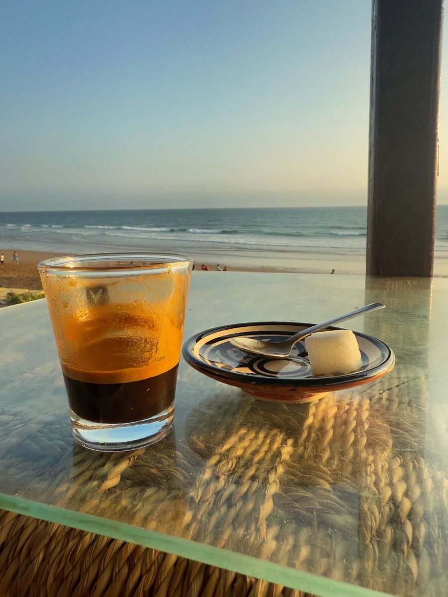 A glass of coffee on a table overlooking the beach