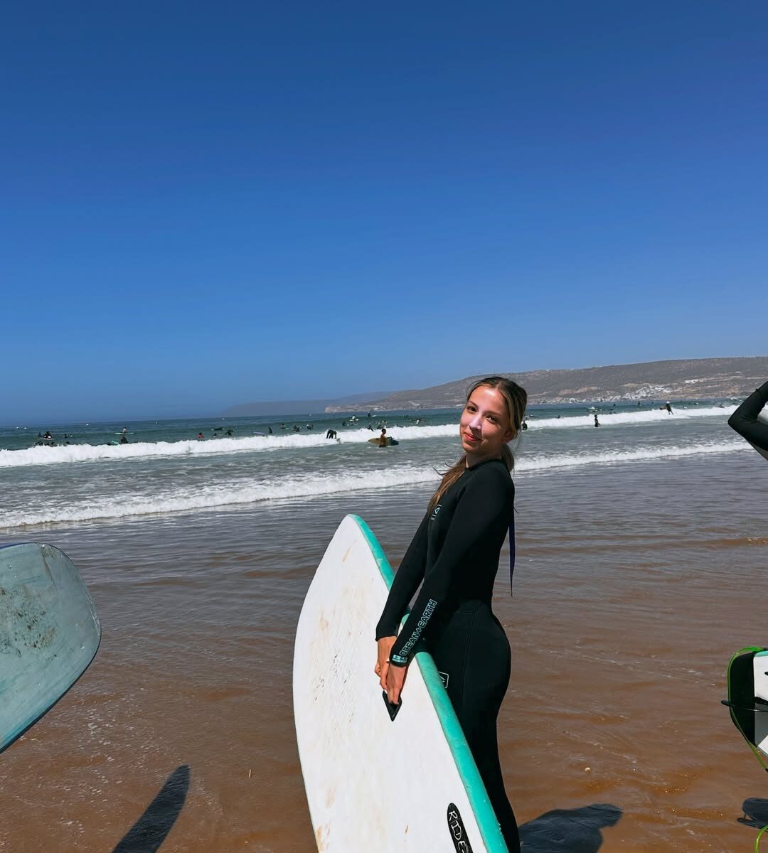 A surfer carrying a white and turquoise board on the beach