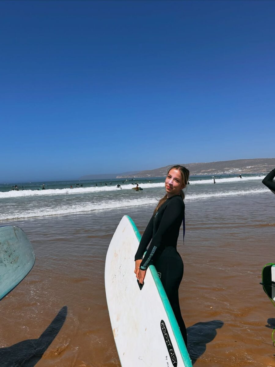 A surfer carrying a white and turquoise board on the beach